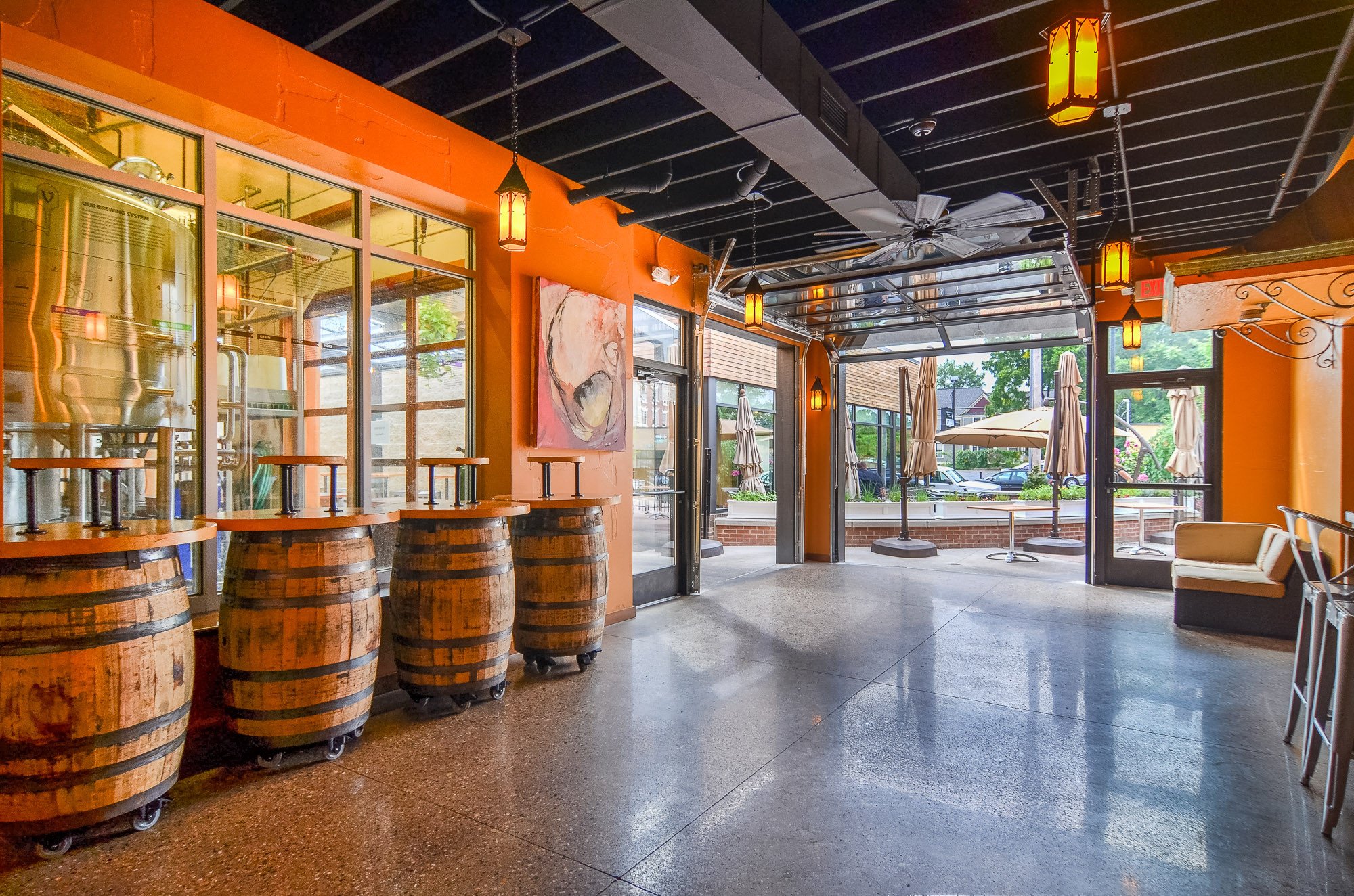 Interior of Walloon Room with barrel tables, orange wall with window to brewery and glass garage door on far end.